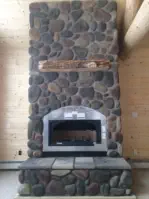 large rock chimney inside of home with log beams